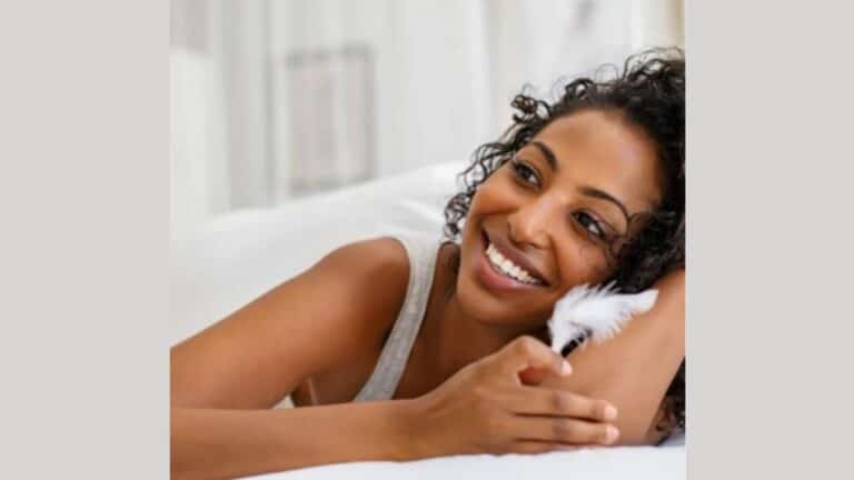 Smiling woman lying on bed holding feather