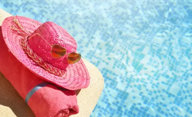 Pink straw hat and sunglasses by swimming pool