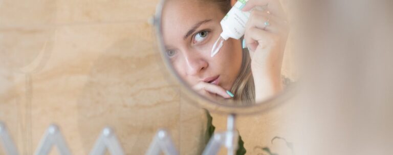 Woman applying eye cream while looking in mirror