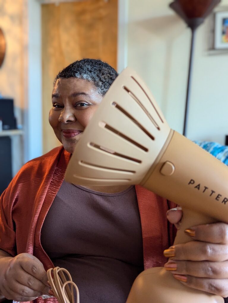 Smiling woman holding beige handheld hair dryer indoors