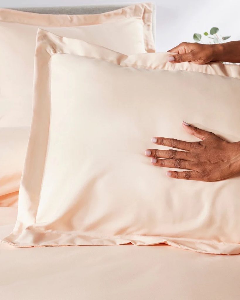 Hands holding peach satin pillowcase on bed
