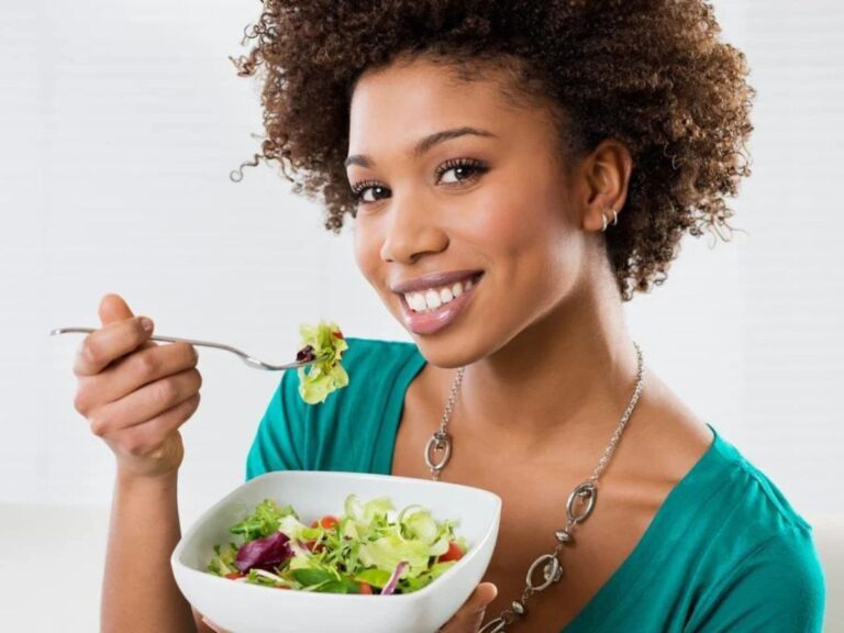 Smiling woman eating fresh green salad from bowl