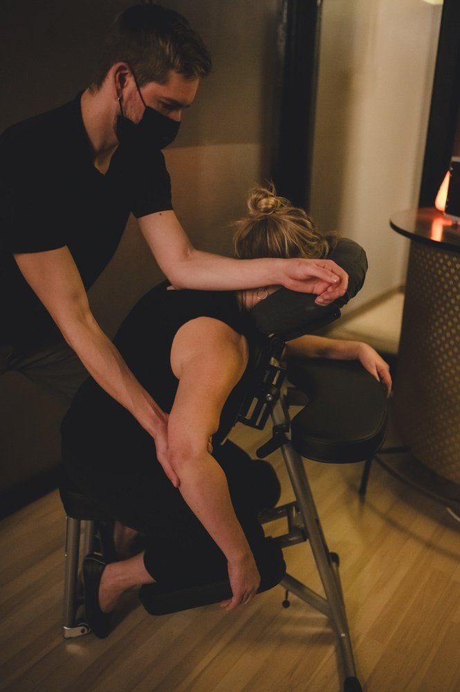 Masked therapist giving seated massage indoors