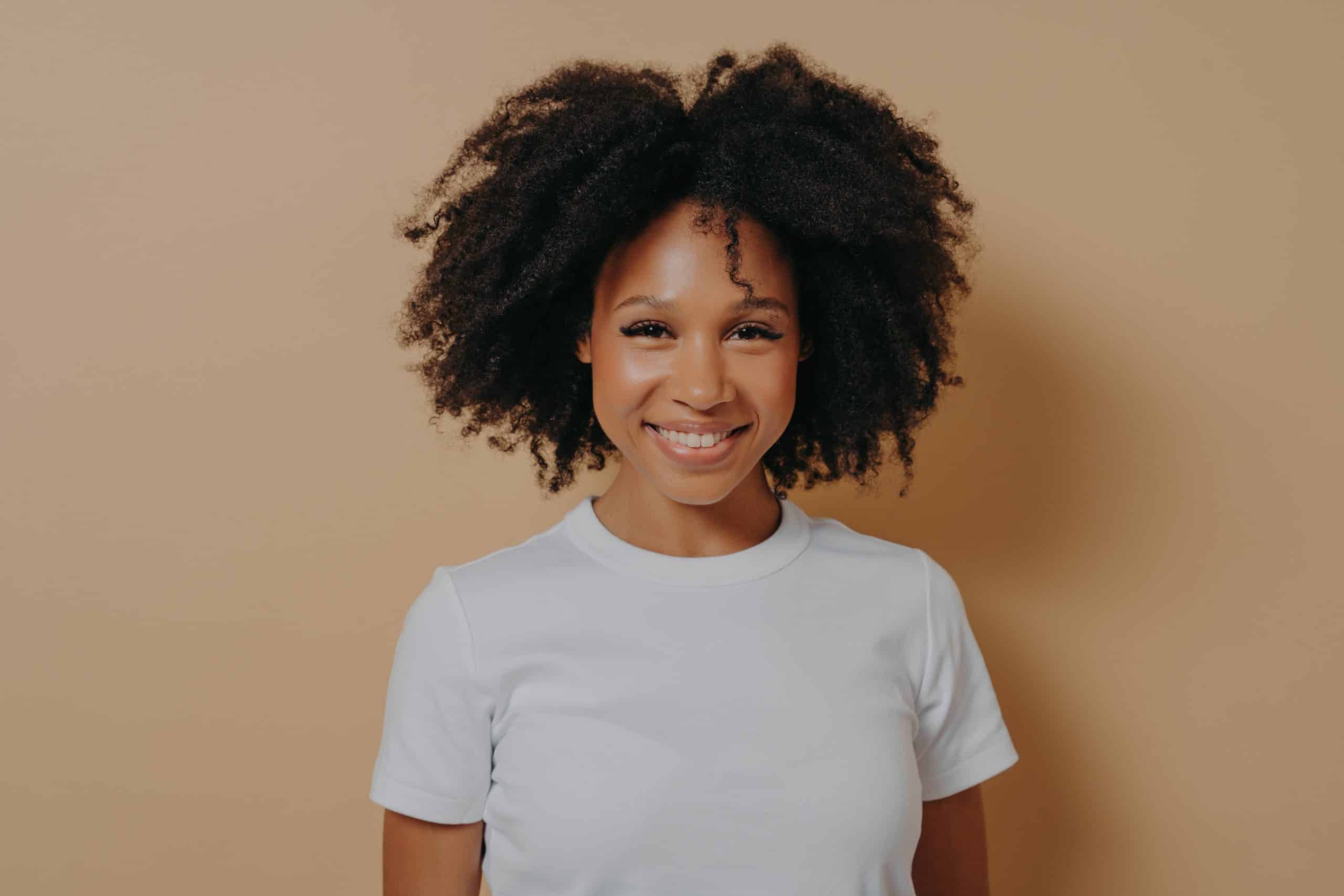 Smiling woman with curly hair on beige background