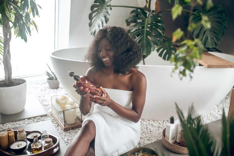 Woman in towel holding bath oil by tub