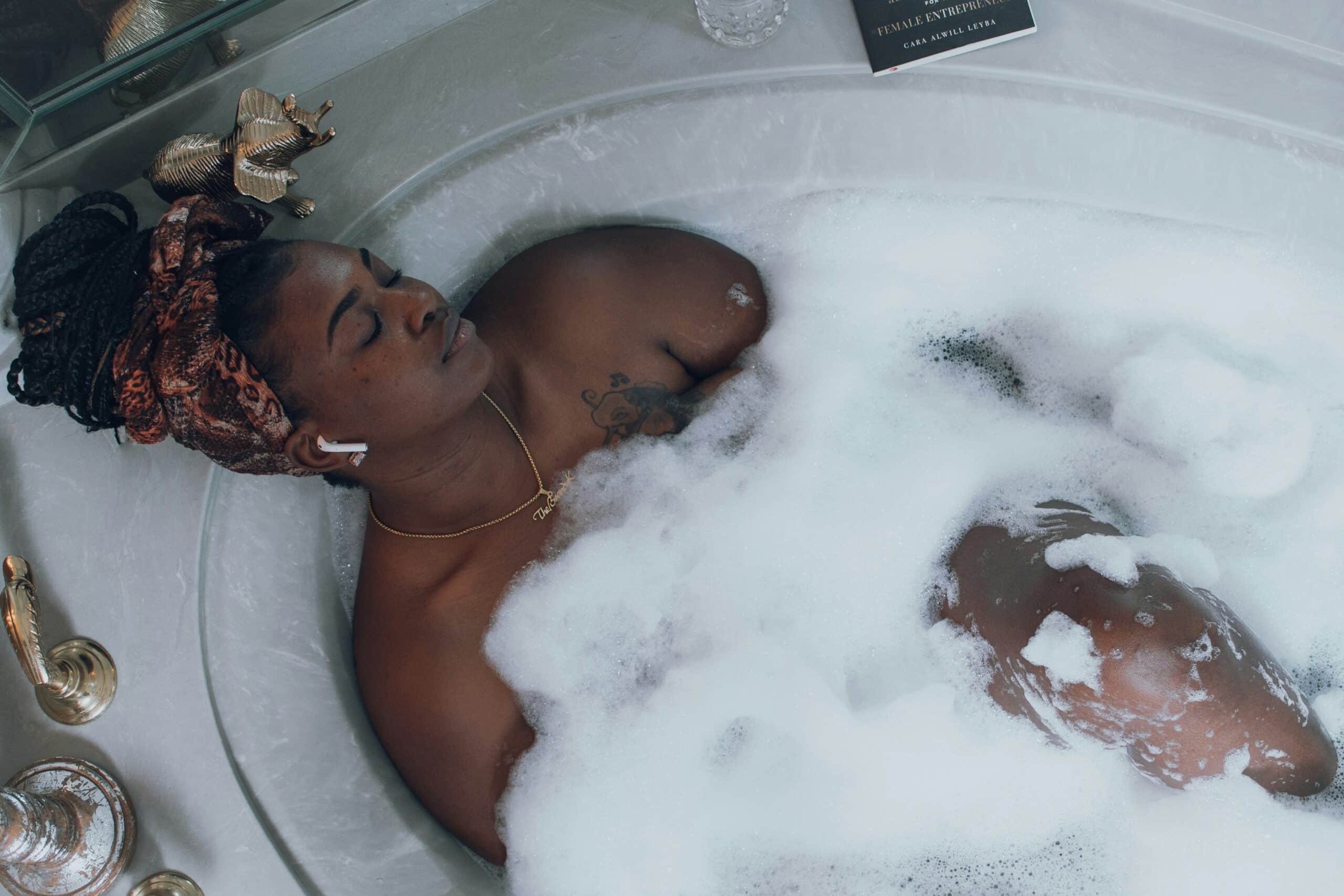 Woman relaxing in bubble bath wearing headwrap and earbuds