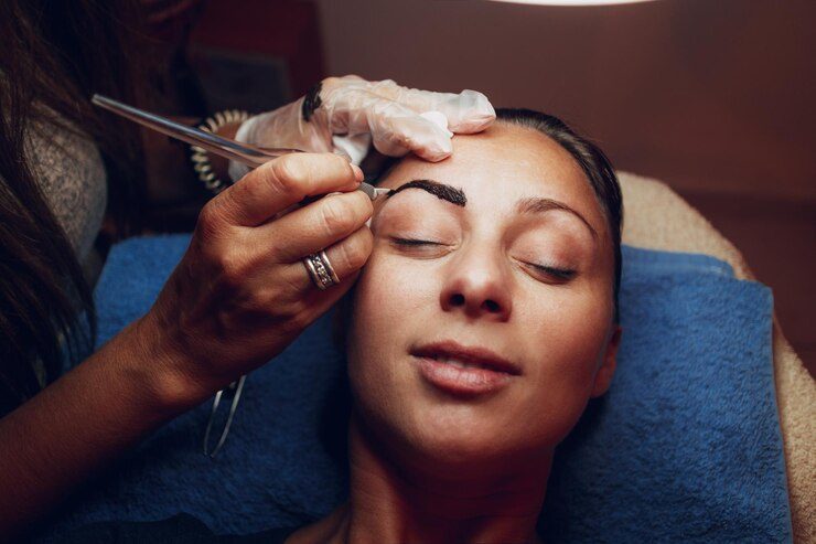 Beautician performing eyebrow microblading on relaxed woman